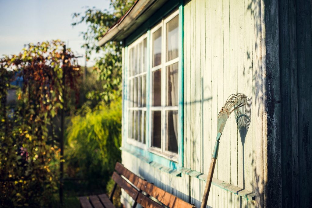 râteau de jardin appuyé sur un mur en bois blanc à l'heure du déjeuner