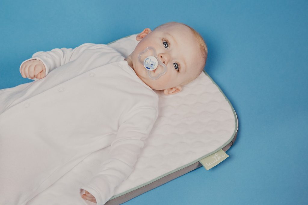 bébé en grenouillère blanche allongé sur le lit