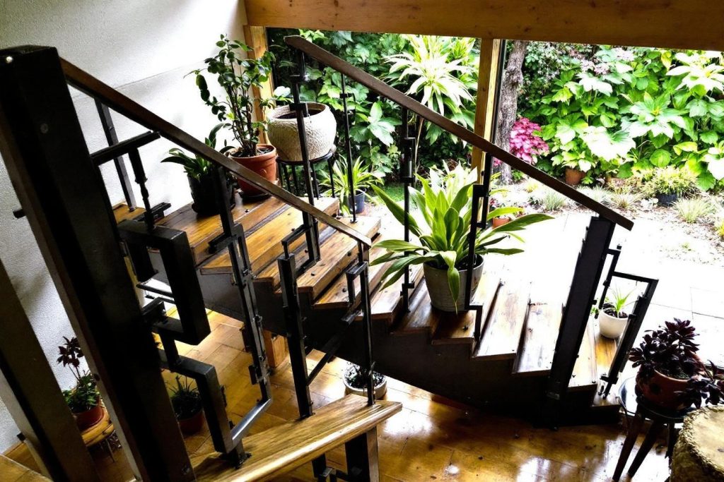 Escalier en bois avec rampe noire et plantes vertes sur les marches